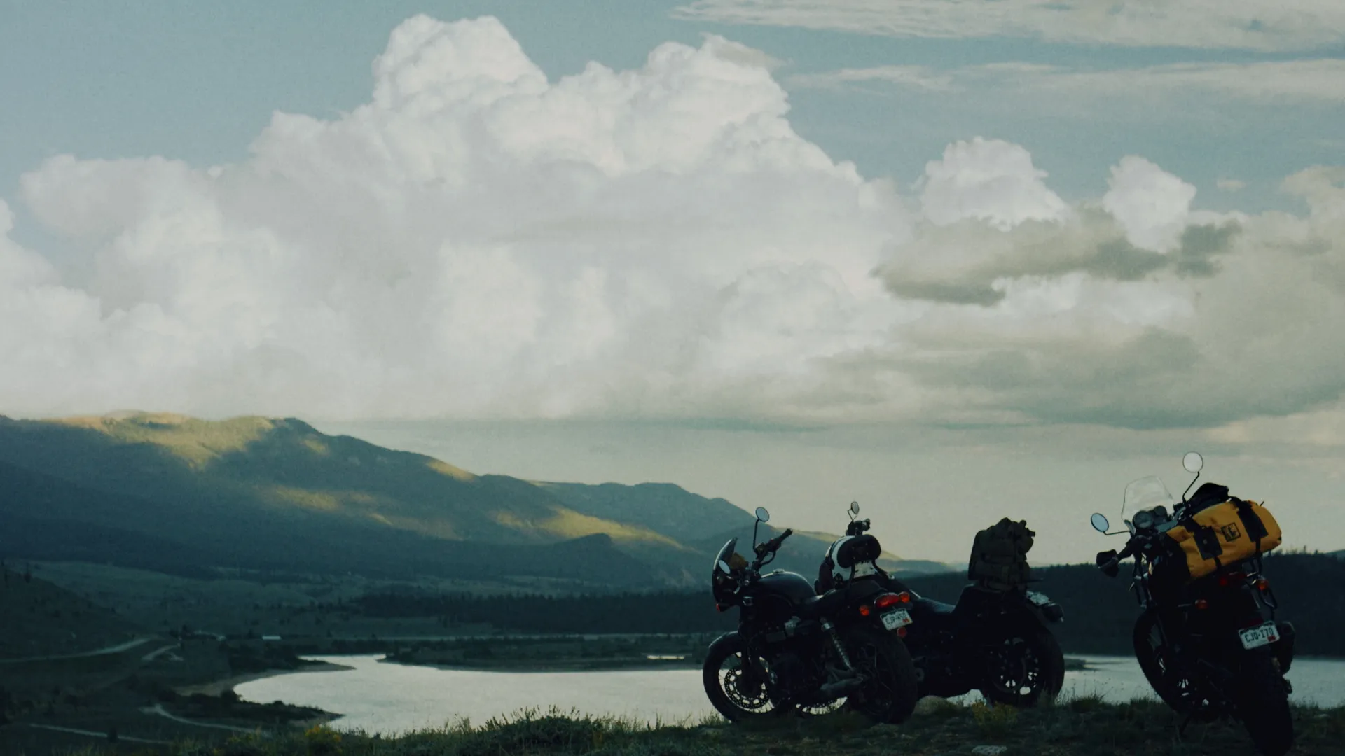 Motorcycles parked at an overlook with clouds over a valley lake