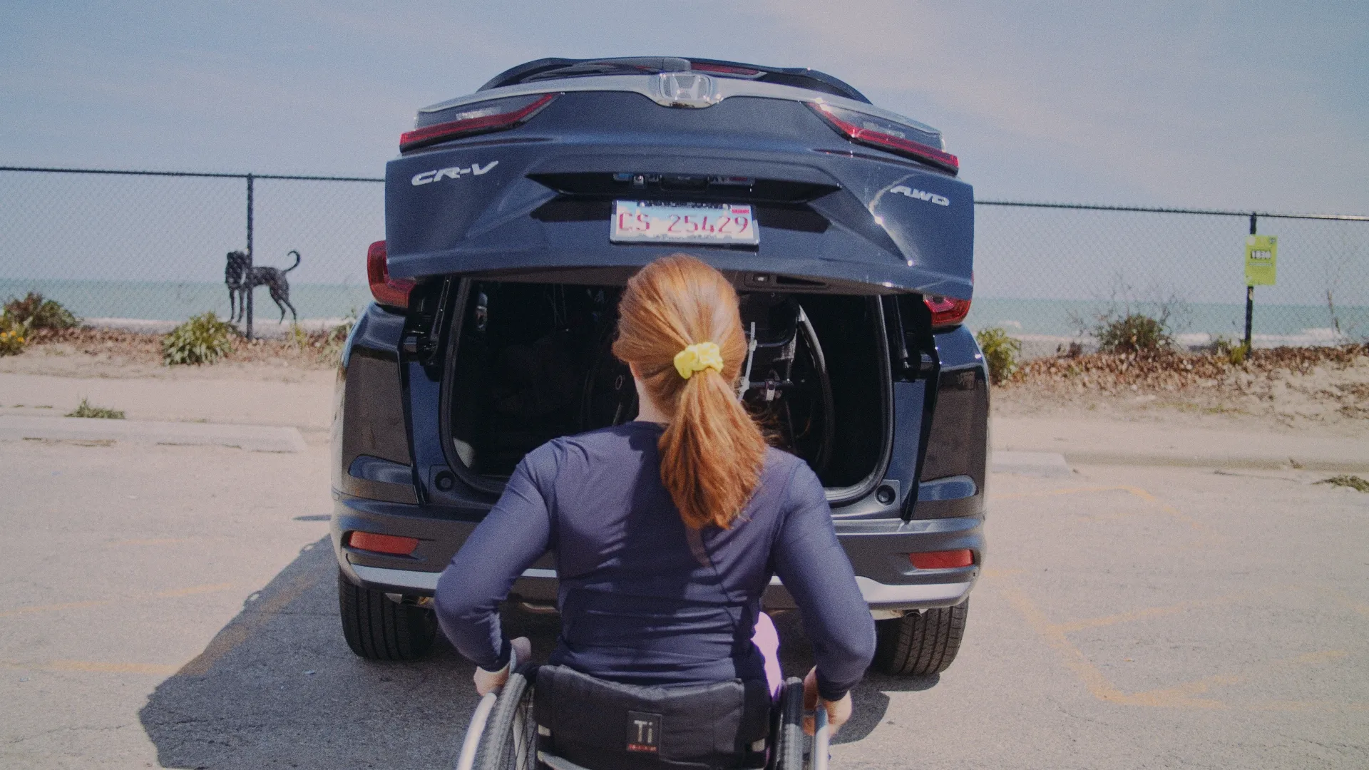 Athlete transferring from a car into a racing wheelchair in a beach parking lot