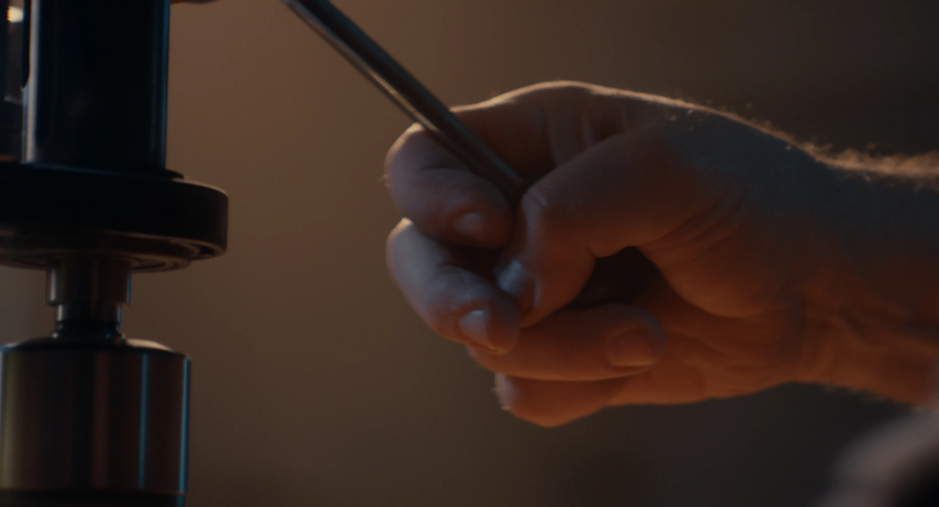 Luthier's hand holding a round file beside a drill press