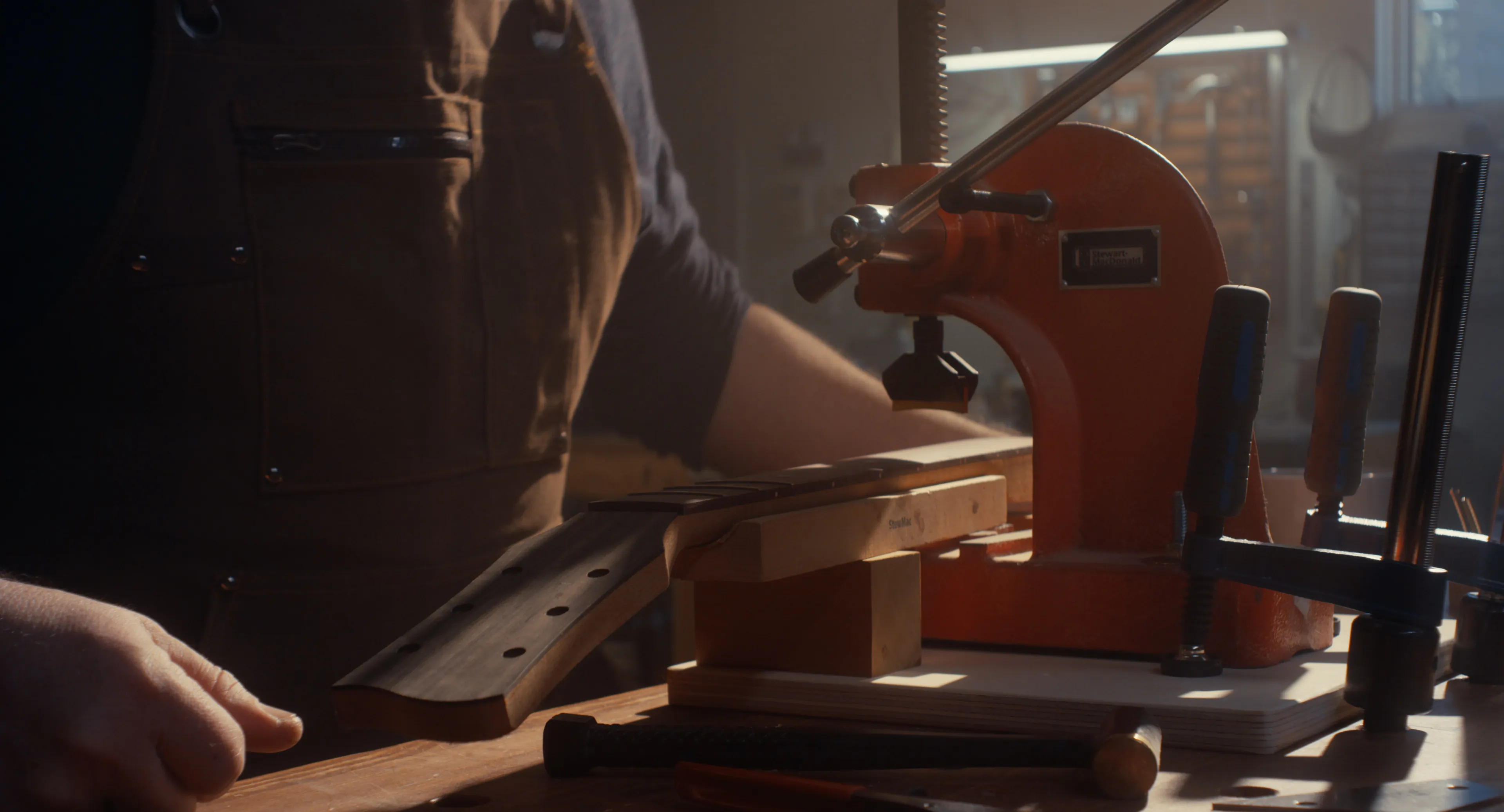Luthier working at a fret press with tools on the bench