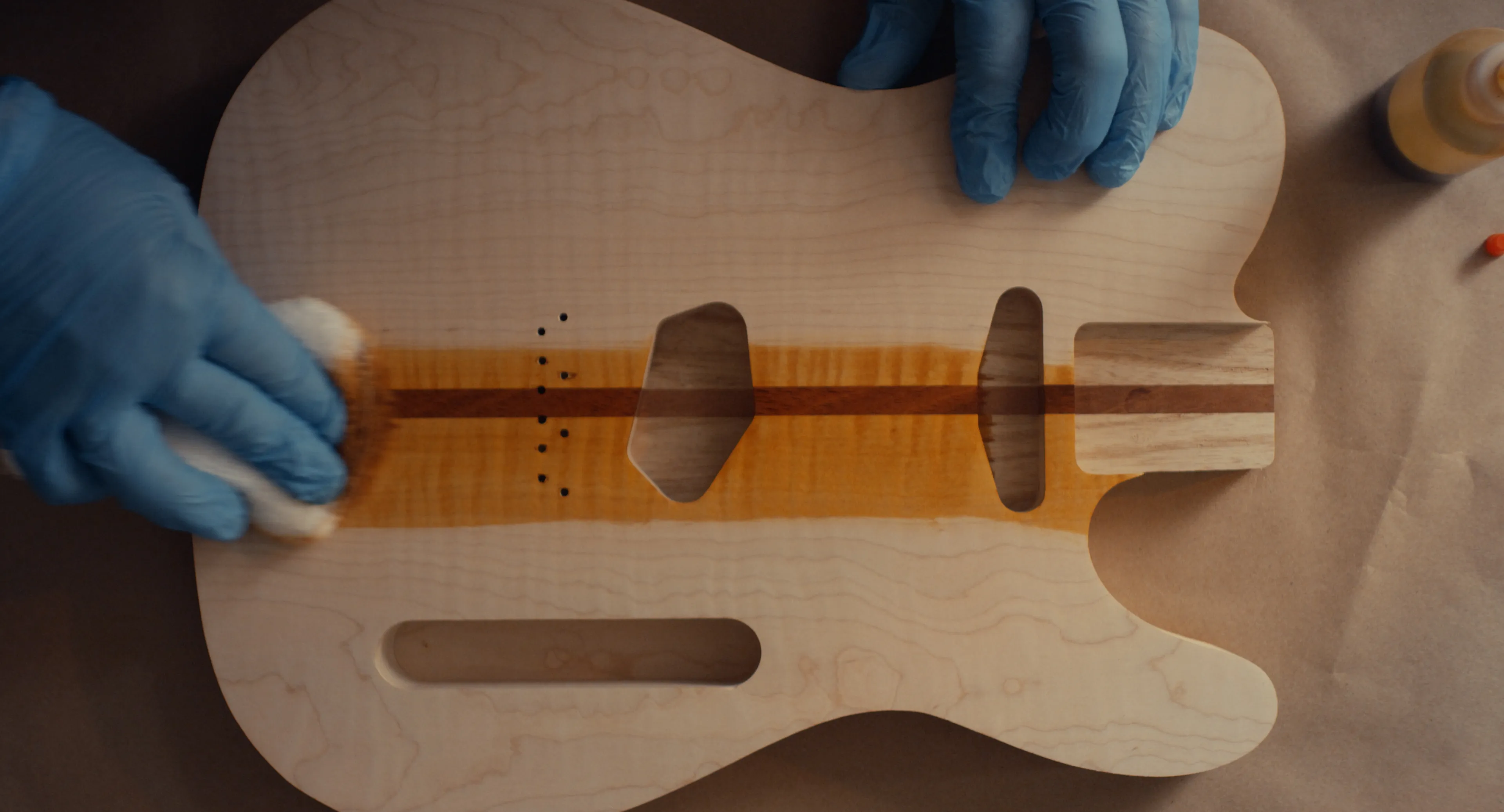 Gloved hands wiping finish onto a flame maple guitar body