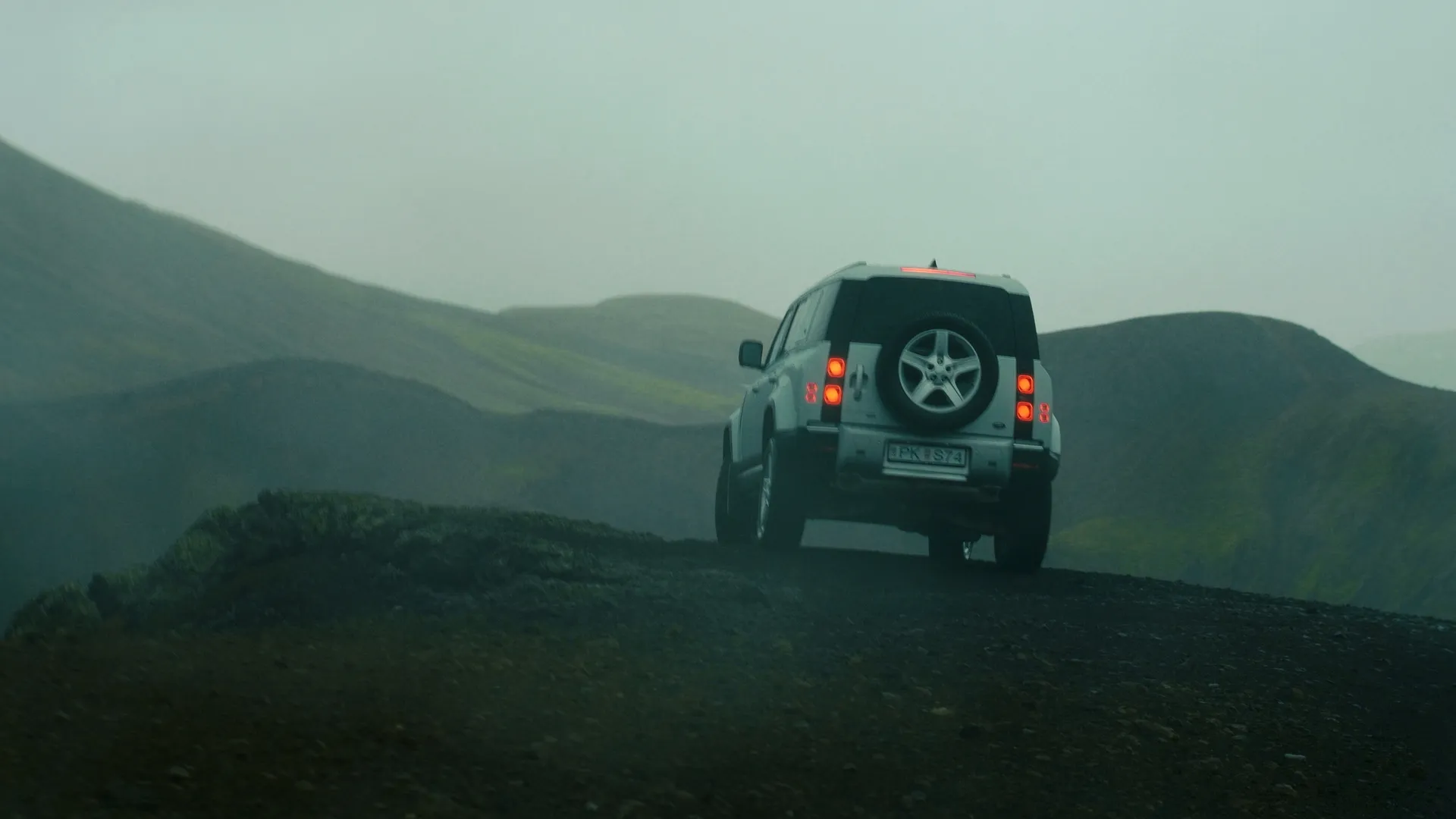 Land Rover Defender from behind on a ridge road in misty green highlands