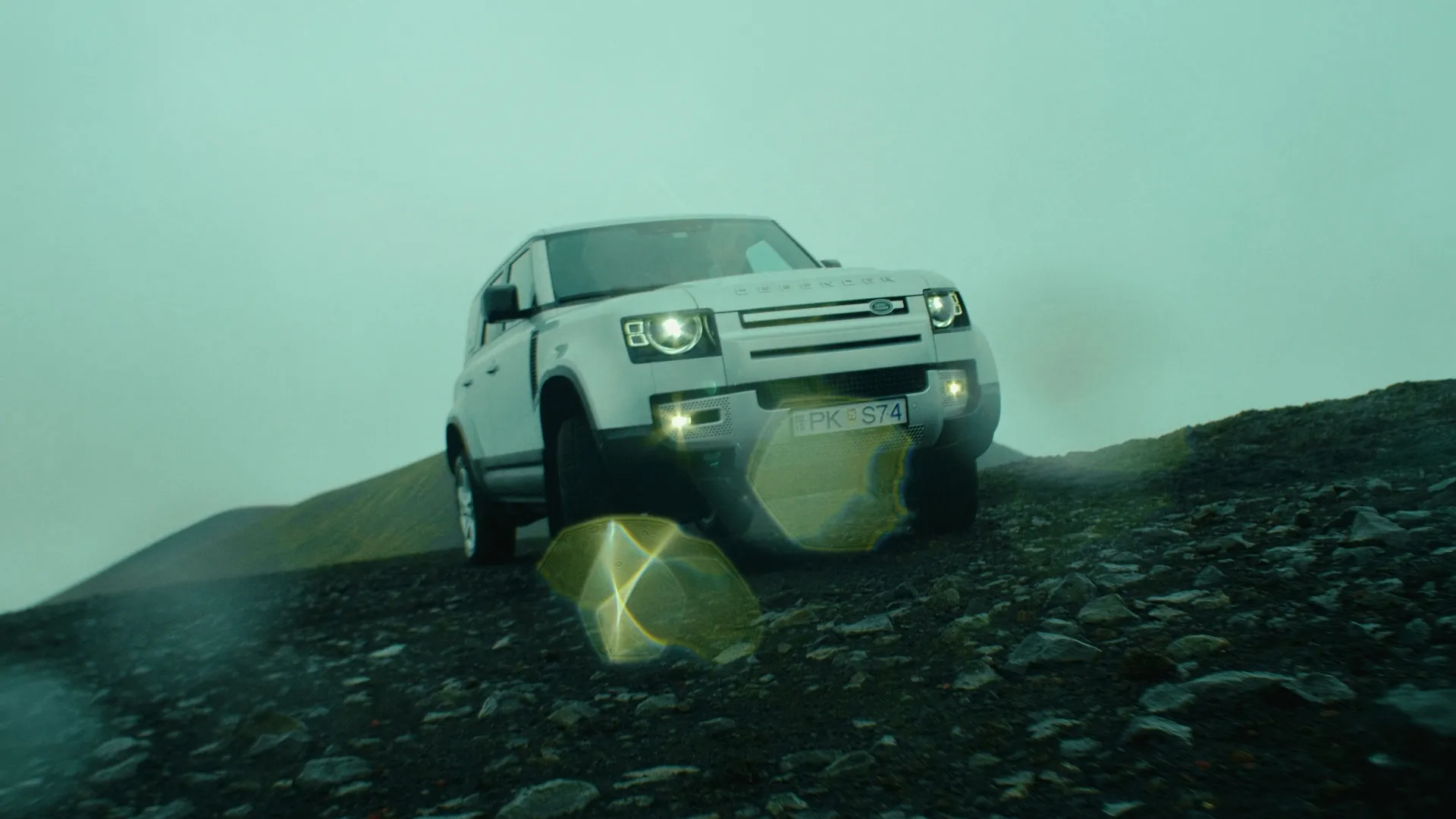Defender climbing a rocky slope head-on in the mist with headlights on