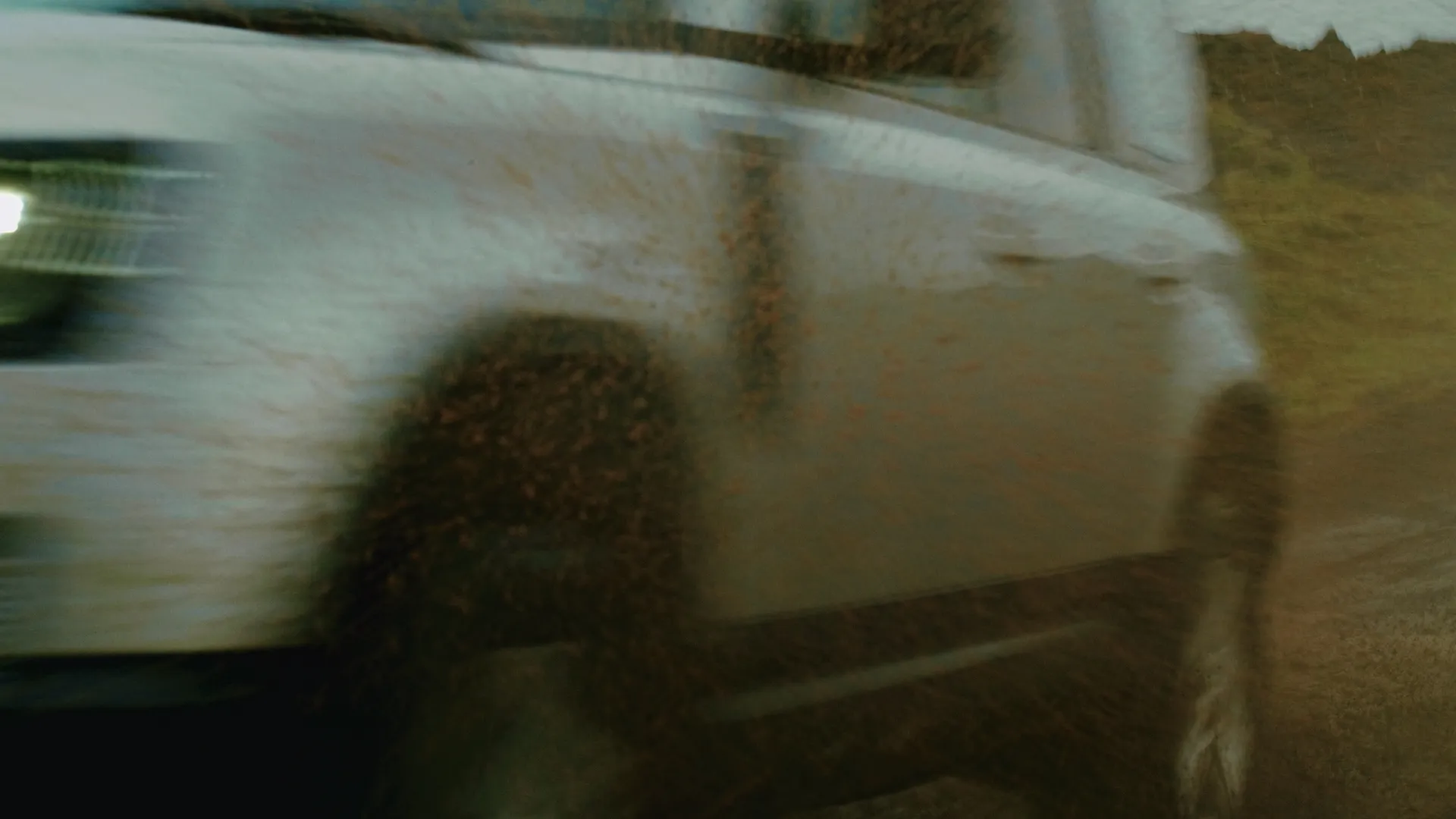 Motion-blurred side of the Defender speeding past on a muddy trail
