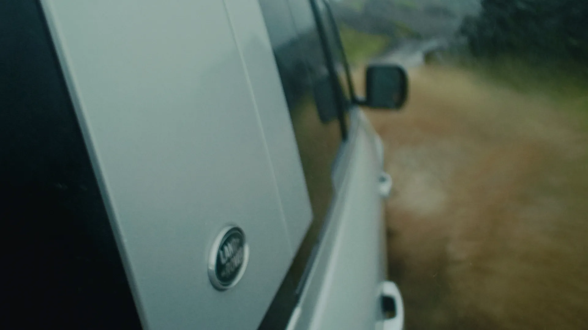 Side of the white Defender with mirror against a muddy trail in motion