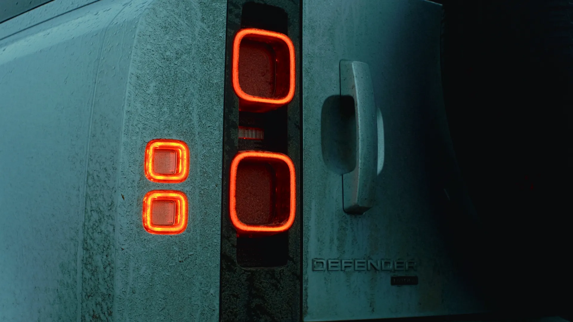 Close-up of the Defender's glowing tail lights on wet white bodywork