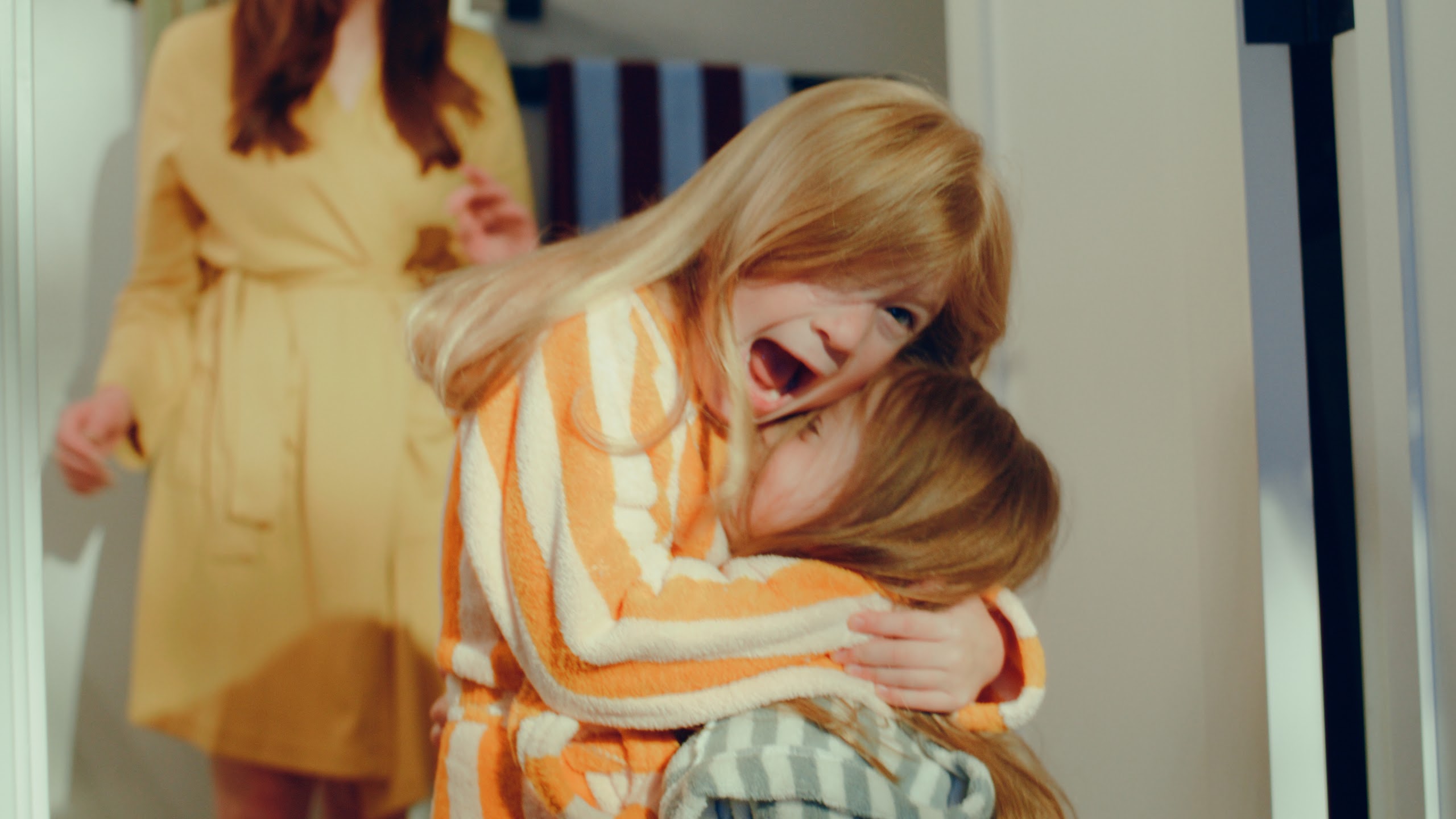 Two sisters laughing and hugging in a sunlit hallway