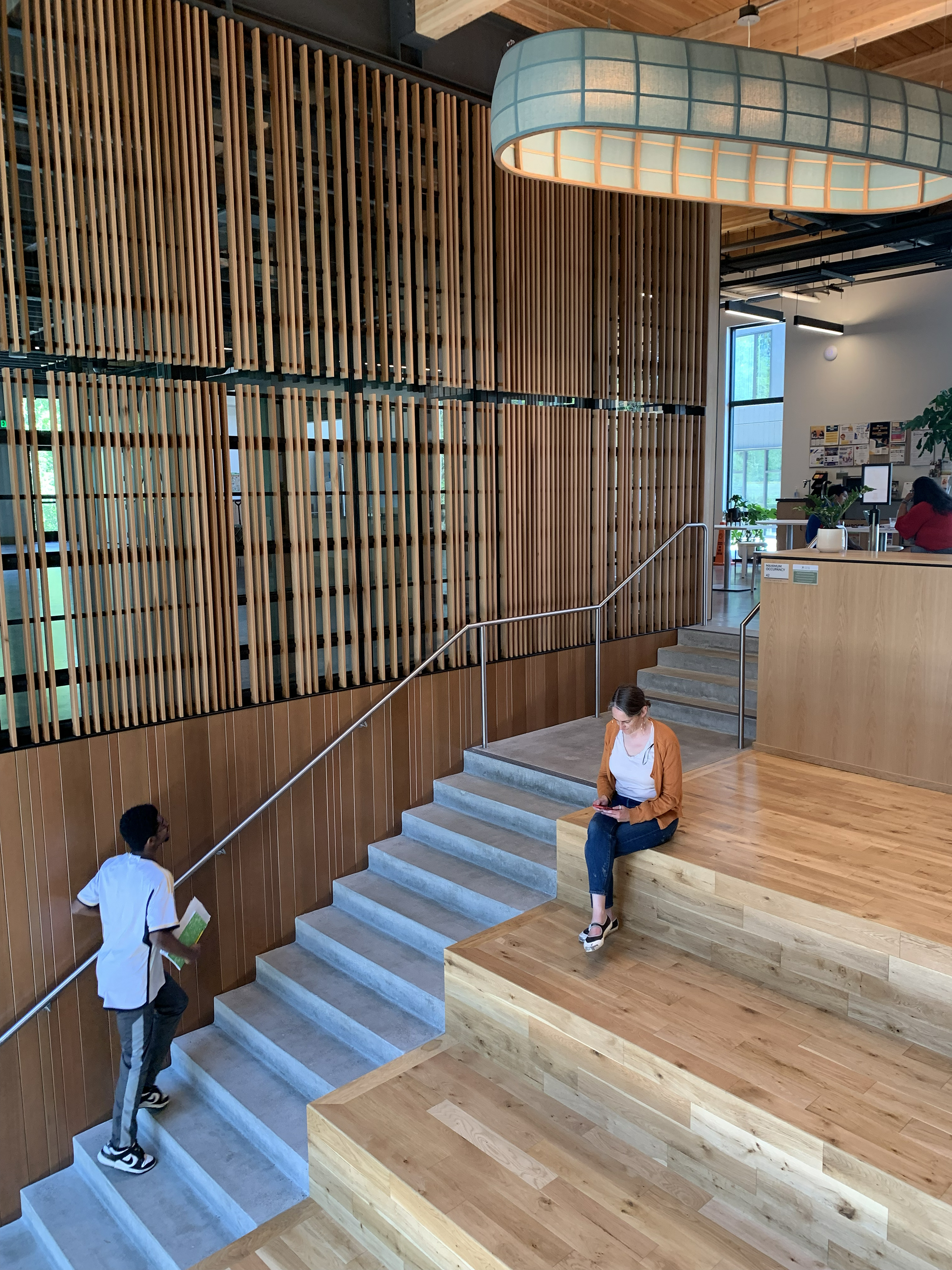 person ascending stairs next to wood clad wall and wood screen on one side and wood stadium stair with person sitting on the other