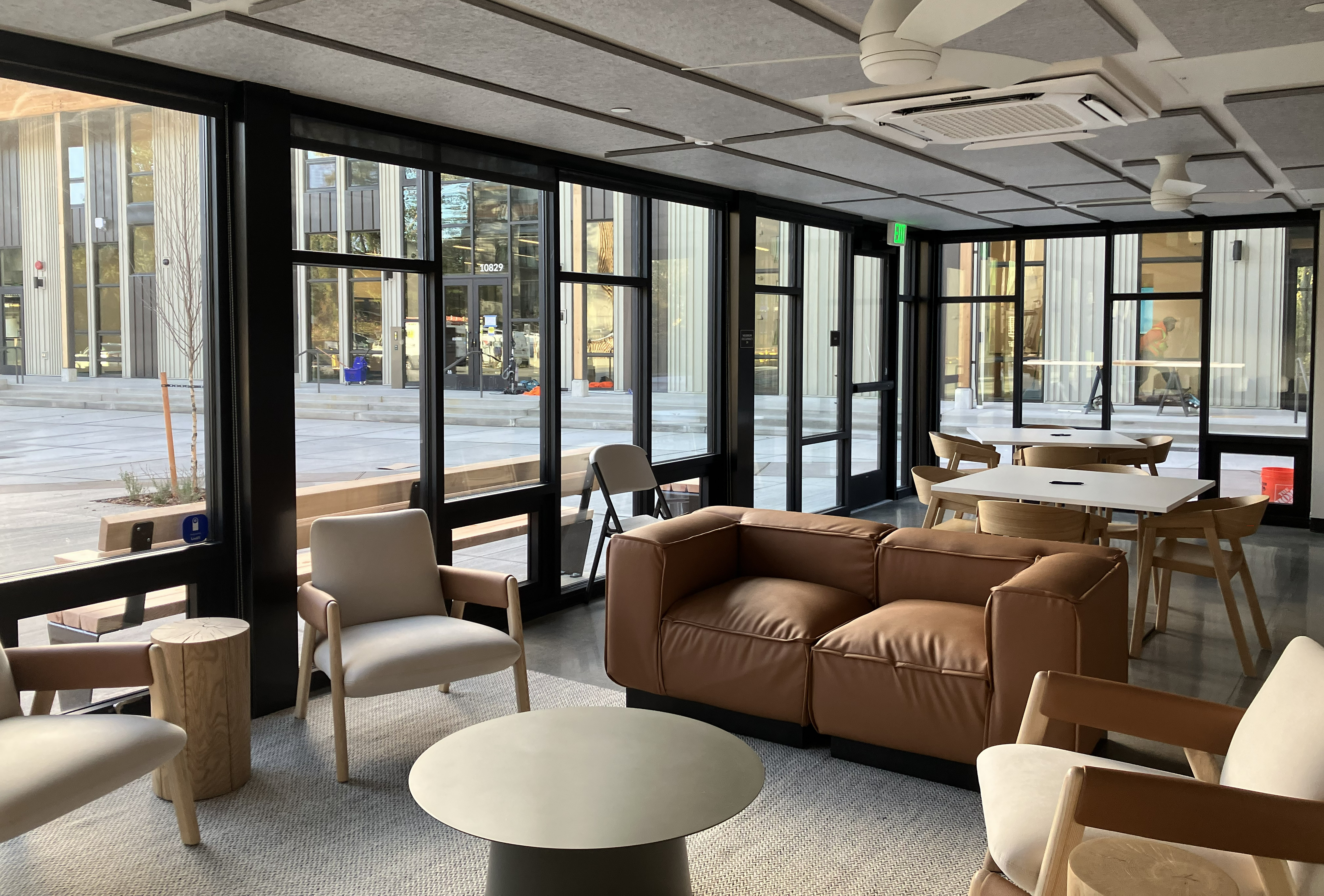 community room in housing building, view of courtyard and community building outside. Comfortable chairs and tables