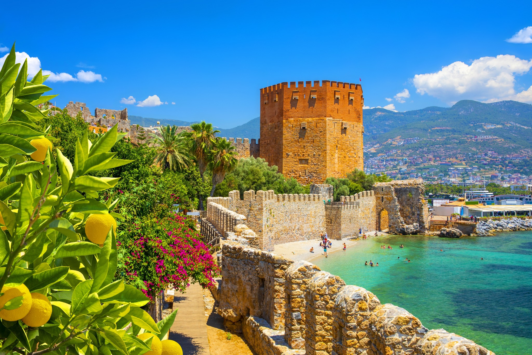 Tourists swimming near the sea walls extending along the coast of Alanya Castle and Red Tower.