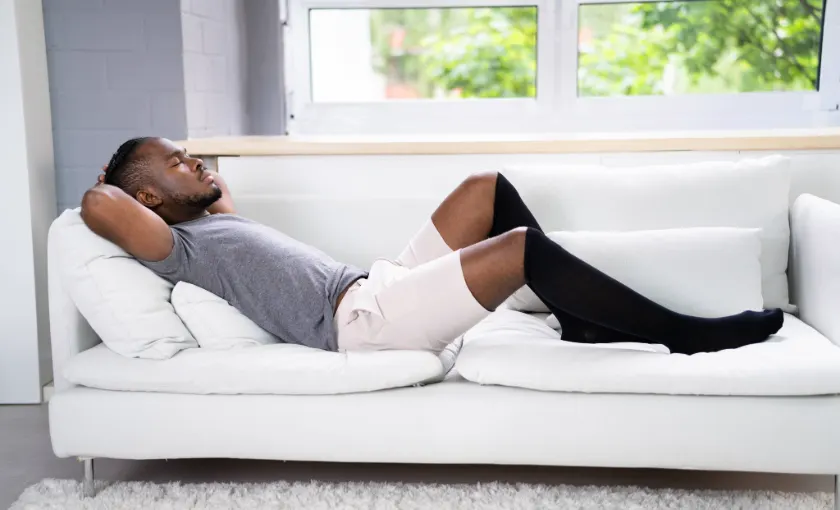 Person elevating legs at home wearing compression stockings to relieve varicose vein symptoms.