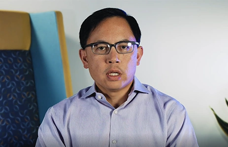 Dr. Brian Chin in front a neutral colored wall, explaining common varicose vein questions.