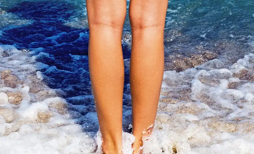 Healthy legs with no visible vein disease standing on the beach