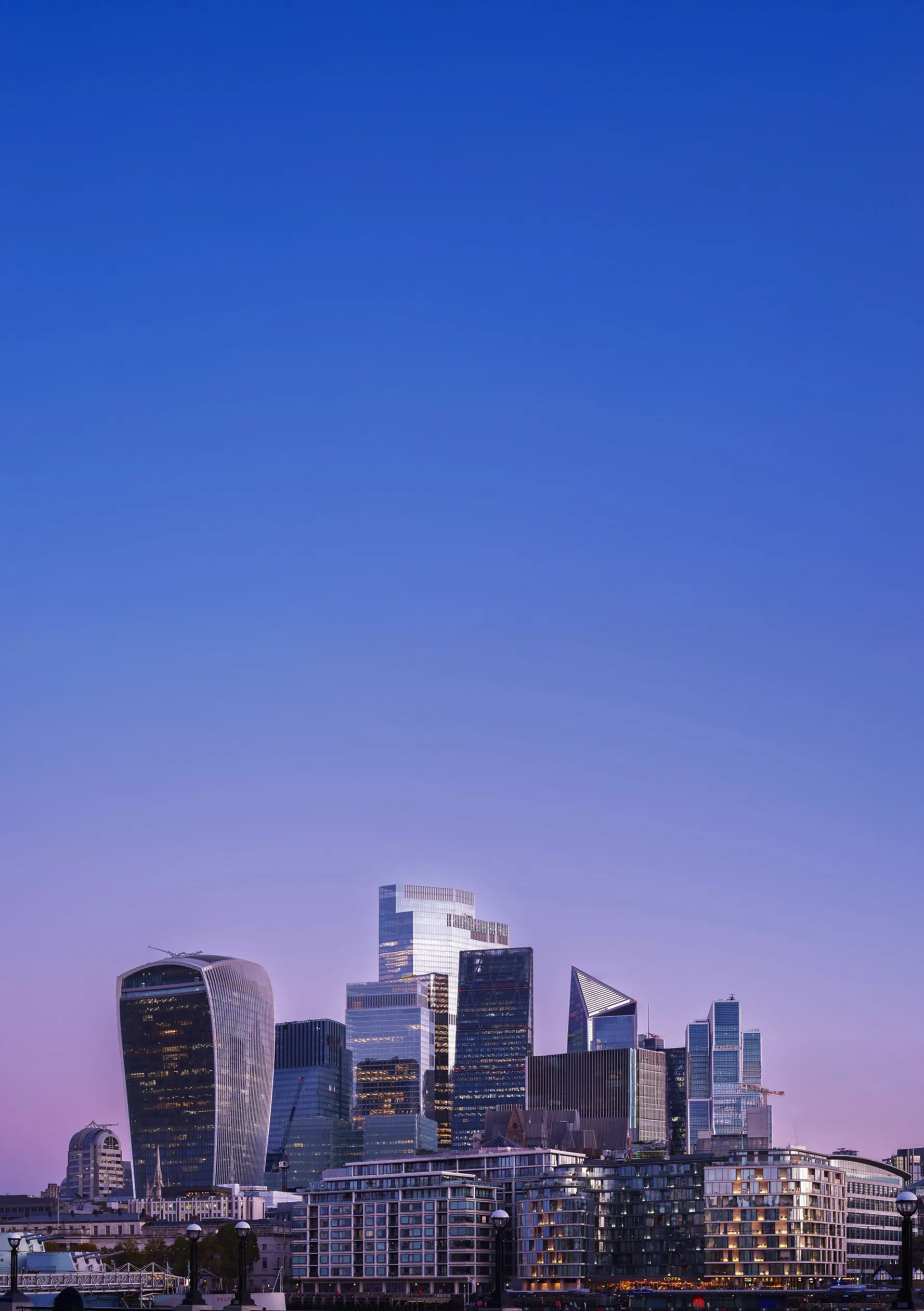 Skyline of modern London skyscrapers including the Walkie Talkie and other tall glass buildings at dusk with a clear blue to purple sky.