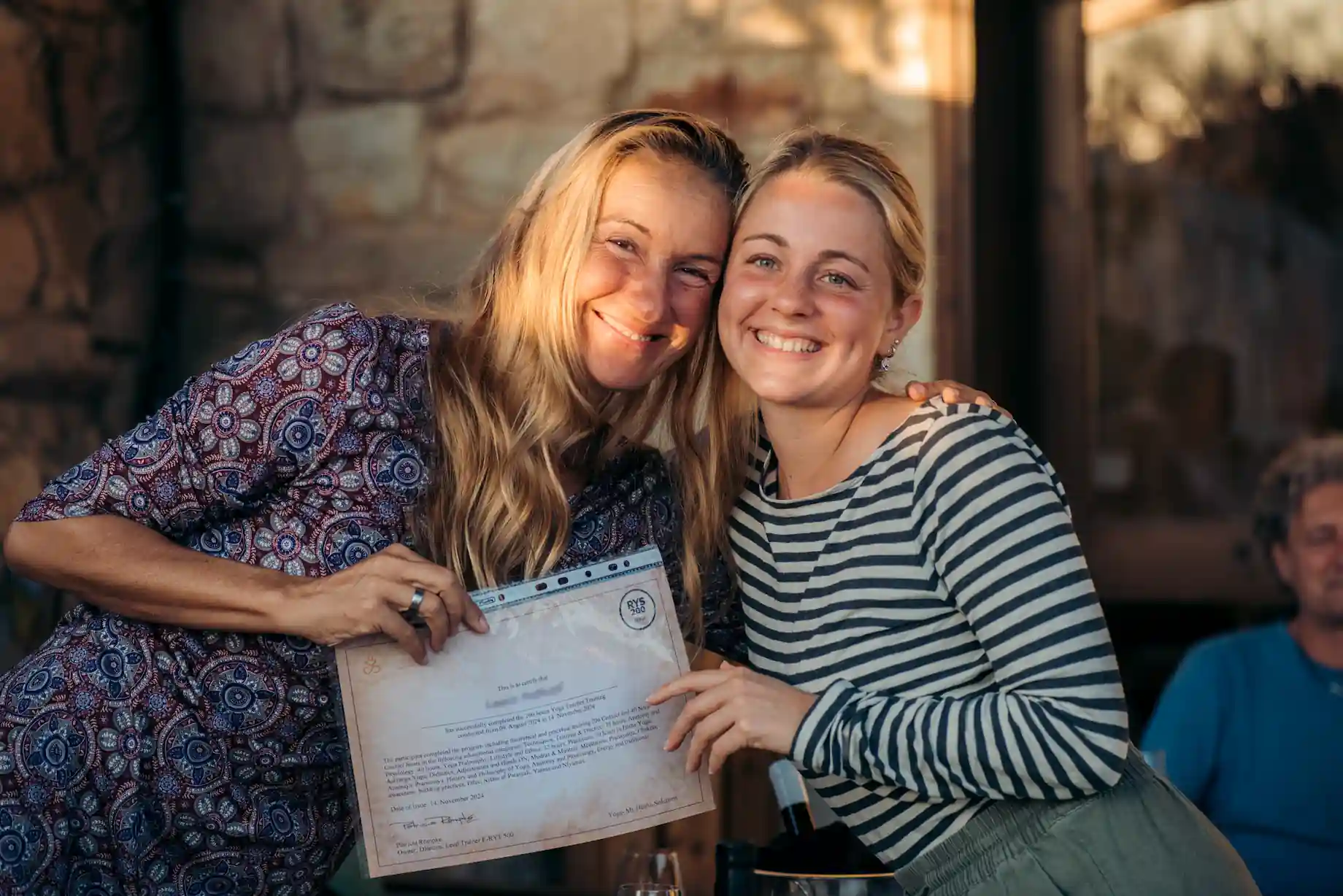 Two women holding a yoga teacher graduation certificate
