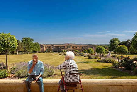 Zwei ältere Menschen sitzen im Garten vor einer Pflegeeinrichtung.