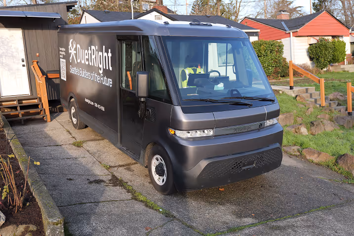 DuetRight branded electric delivery van parked in a residential driveway beside a small house and yard.