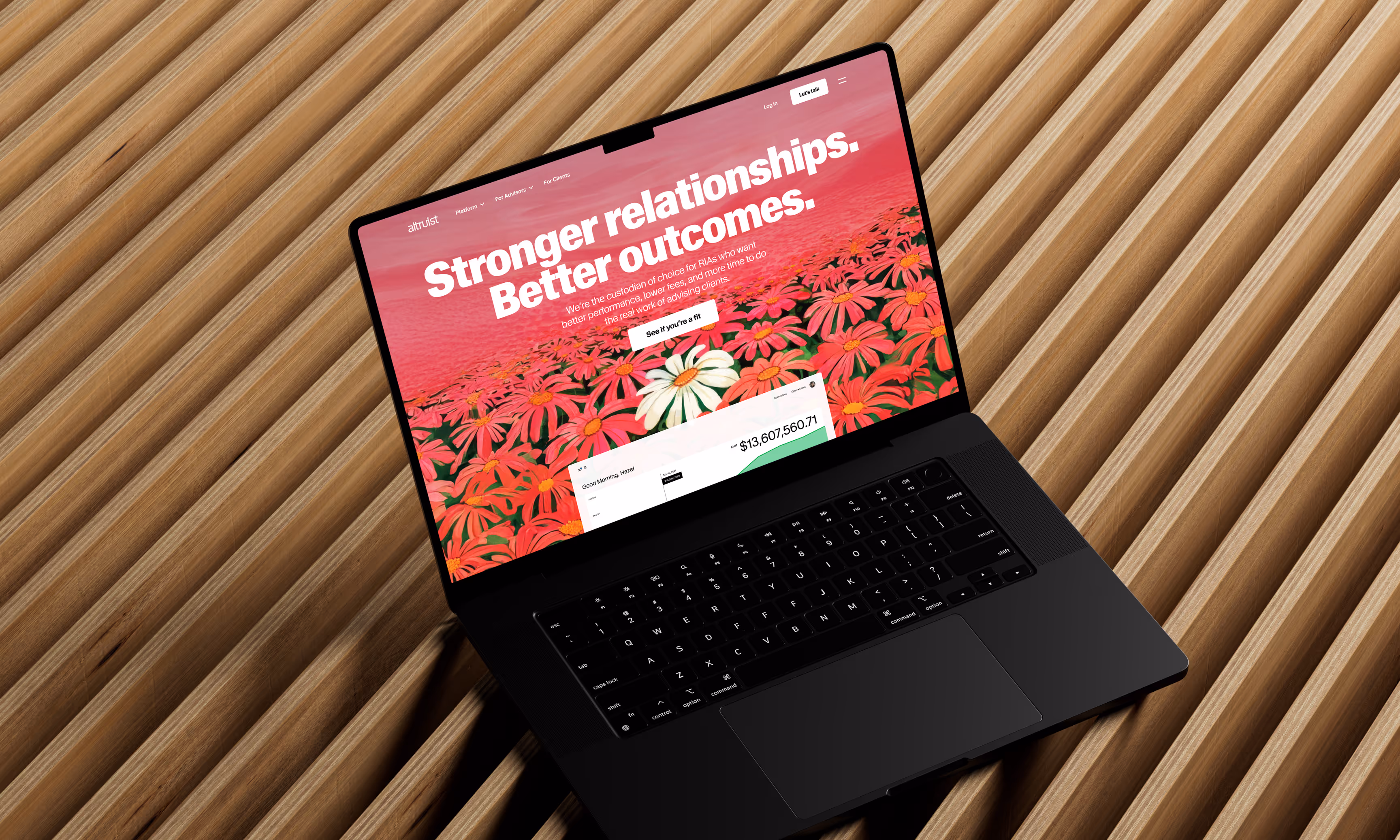 Open black laptop on a wooden slatted surface displaying a website with pink and red flowers and text reading 'Stronger relationships. Better outcomes.'