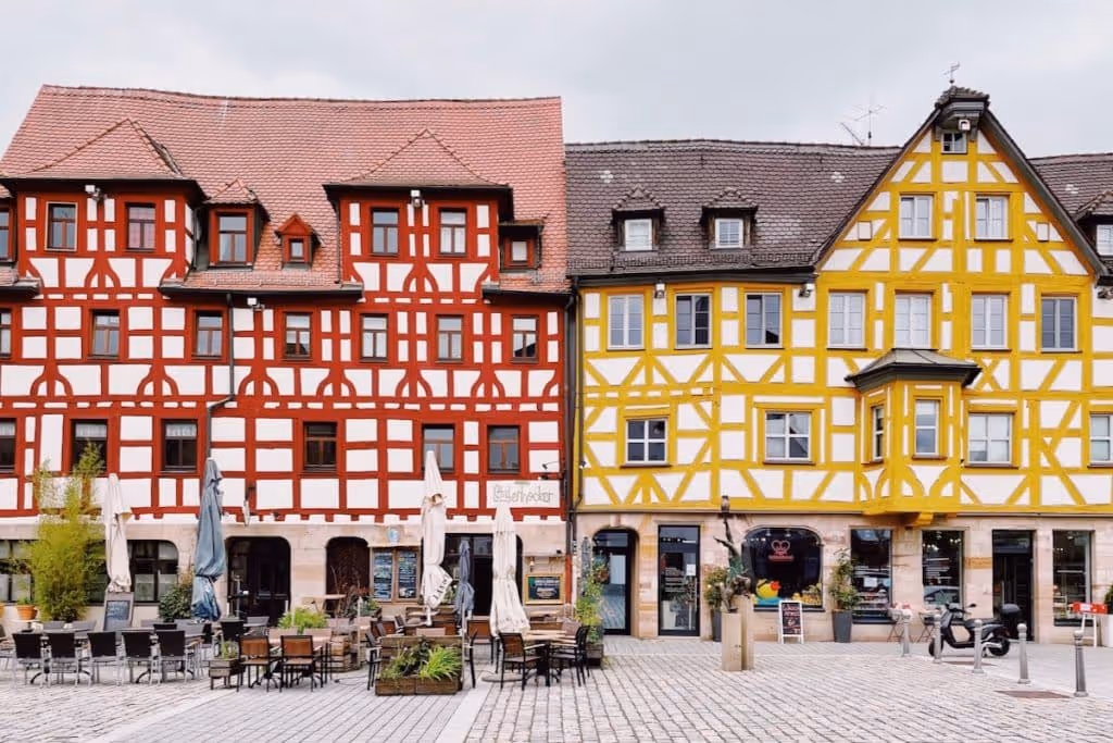 Traditional half-timbered buildings with red and yellow accents and outdoor cafe seating on a cobblestone square.