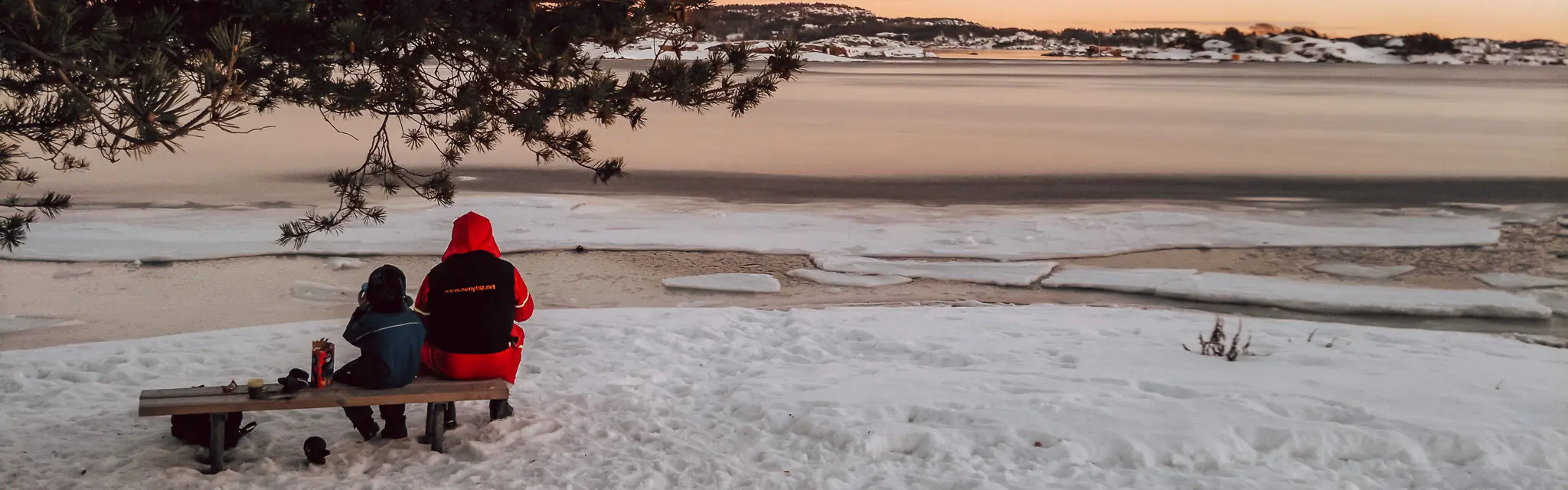 bilde av isdekt fjordlandskap med to personar som sit på ein benk