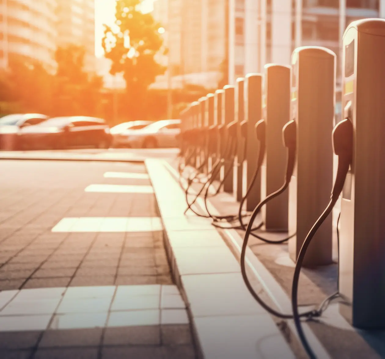 Row of electric vehicle charging stations lined up on a city sidewalk in sunlight.