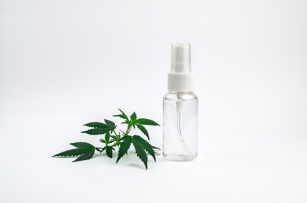 Transparente Sprühflasche neben Cannabisblatt auf weißem Hintergrund – Symbolbild für Cannabis Spray Sativex®