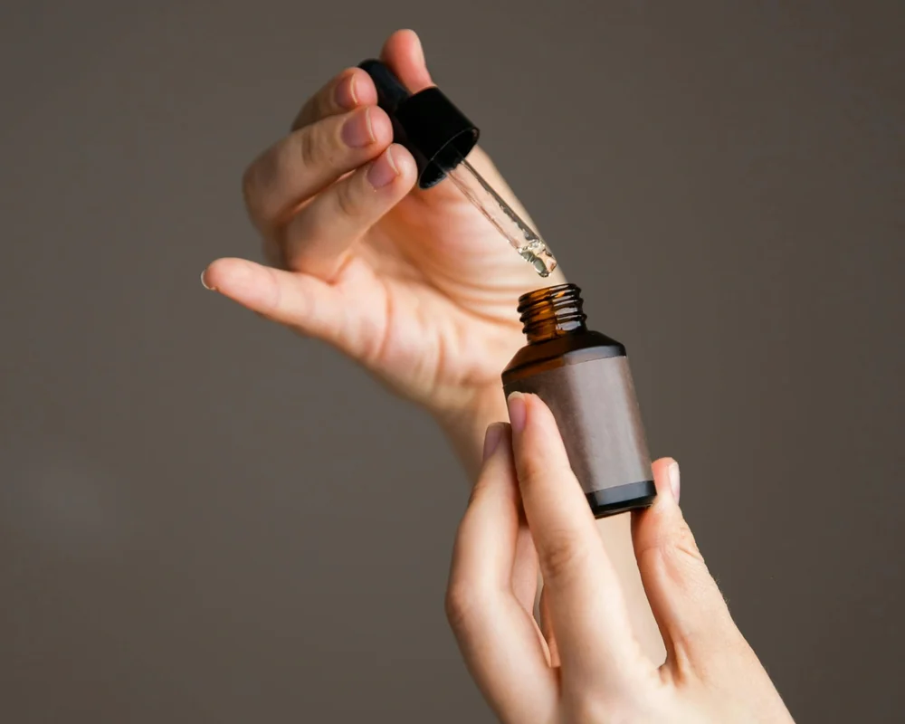 Person hält Pipette mit Öl über braunem Fläschchen – Symbolbild für CBD Cannabidiol