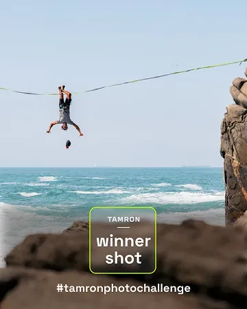 Fotografie eines Slackliners, der kopfüber über dem Meer hängt, mit Felsen im Vordergrund. Beschriftung: ‚Tamron winner shot #tamronphotochallenge‘.