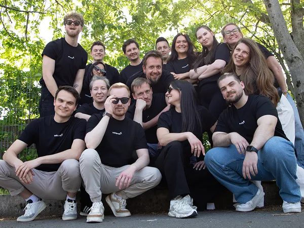 16 Online Marketing Expert:innen für Social, Creation und Performance von adfriends, posen und lachen freundlich in die Kamera. Alle tragen schwarze T-Shirts mit dem Logo darauf.