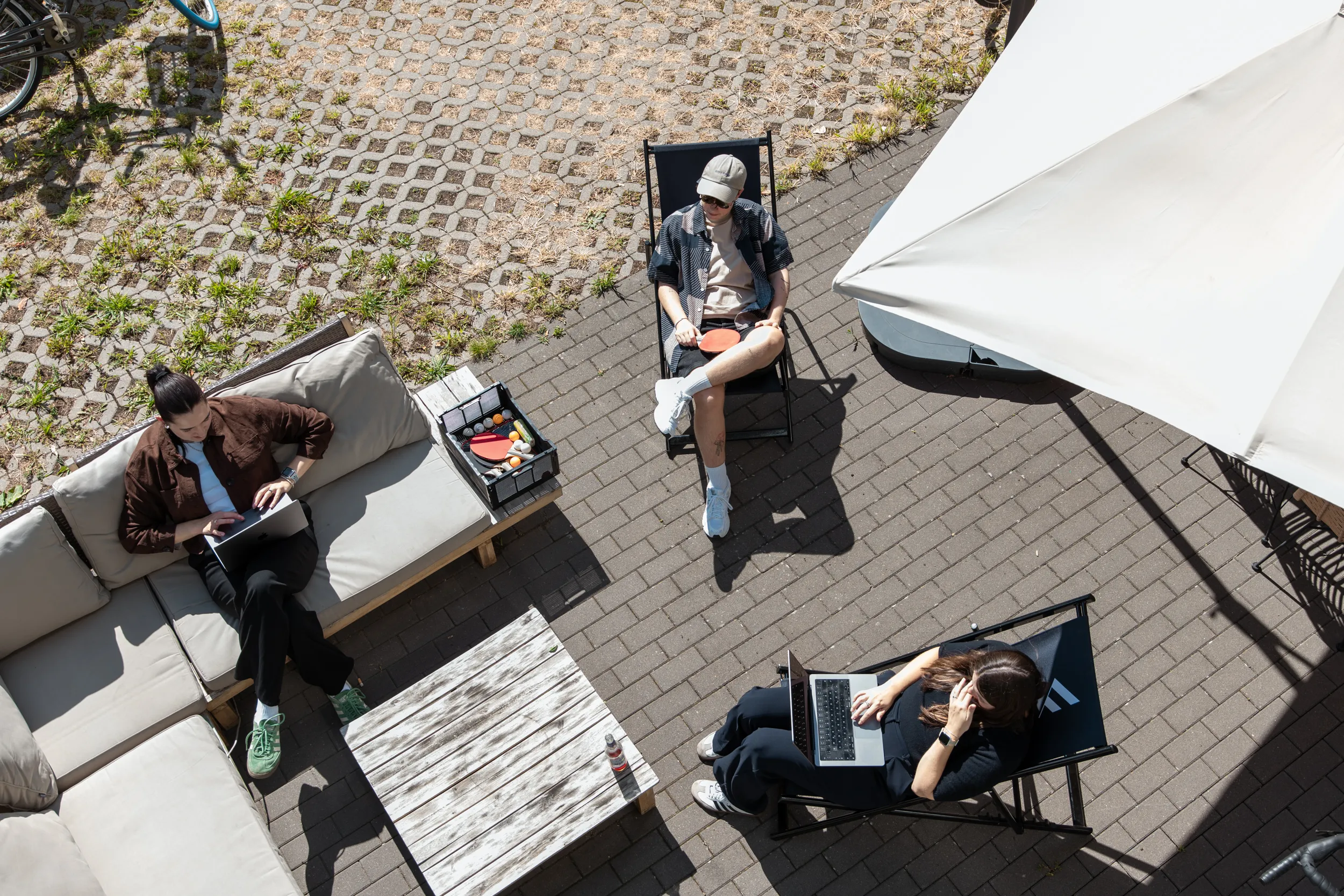 Ein Bild, das in der Vogelperspektive aufgenommen wurde und drei Teammitglieder zeigt, die auf der gemütlichen Terrasse mit Laptops sitzen und im Freien an spannenden Projekten der Online Marketing Agentur arbeiten.