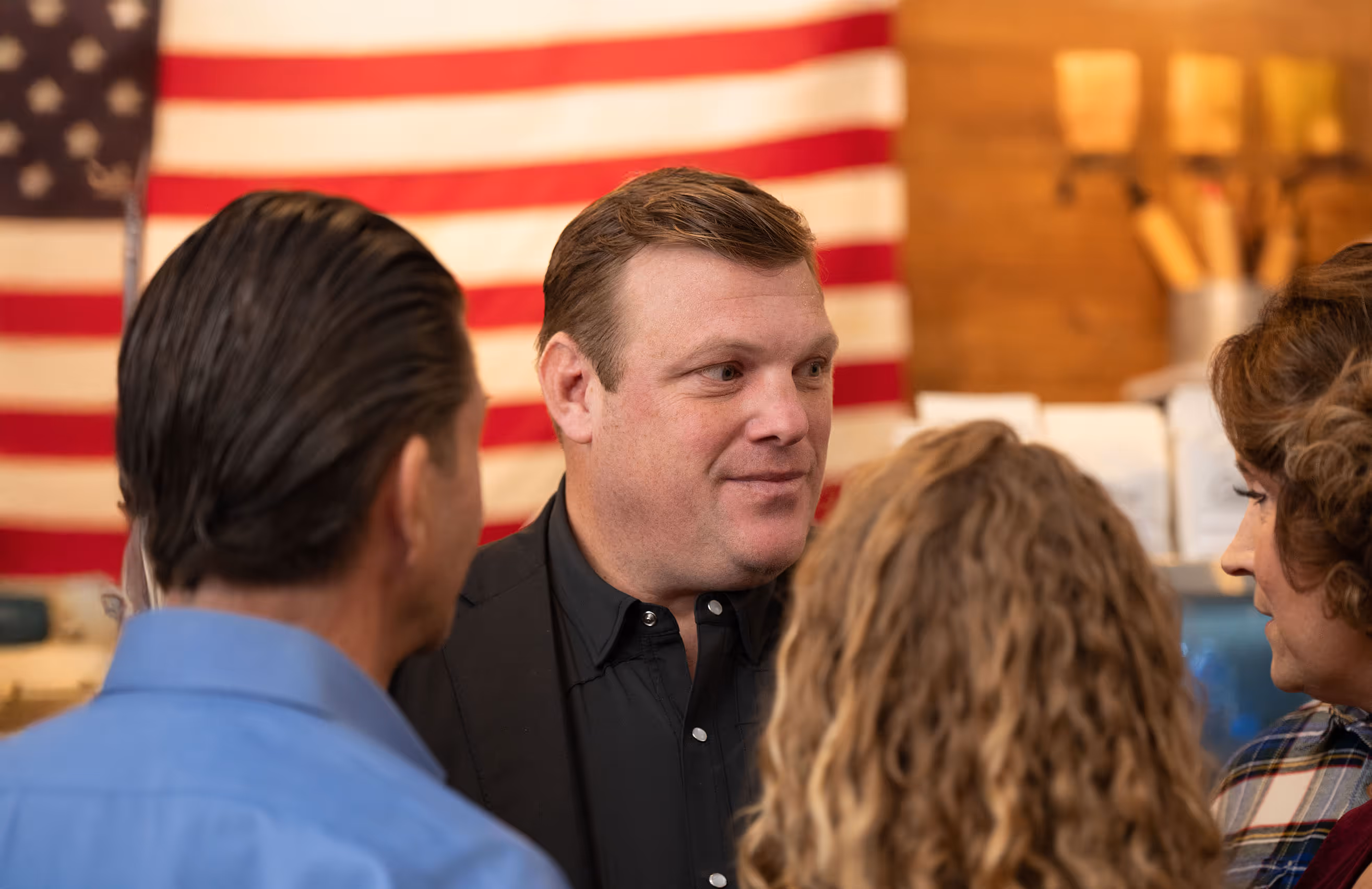 Paul Bondar with other people in conversation with an American flag hanging on the wall in the background.