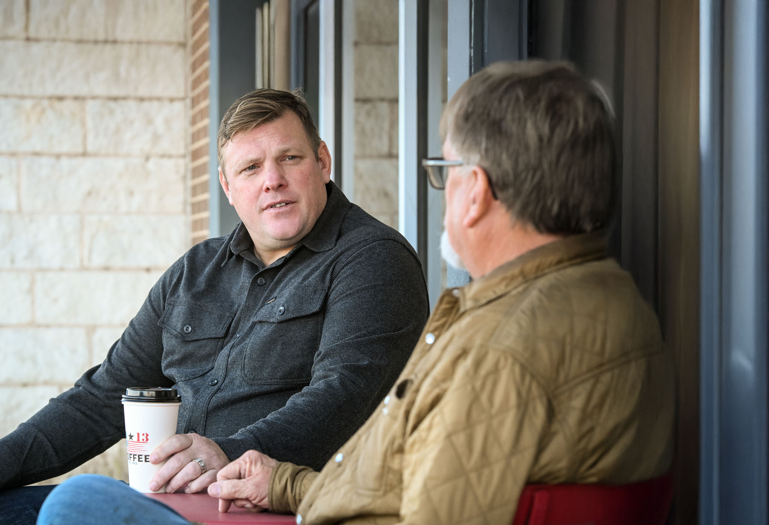 Paul Bondar and another man sitting and having a conversation, one holding a coffee cup.