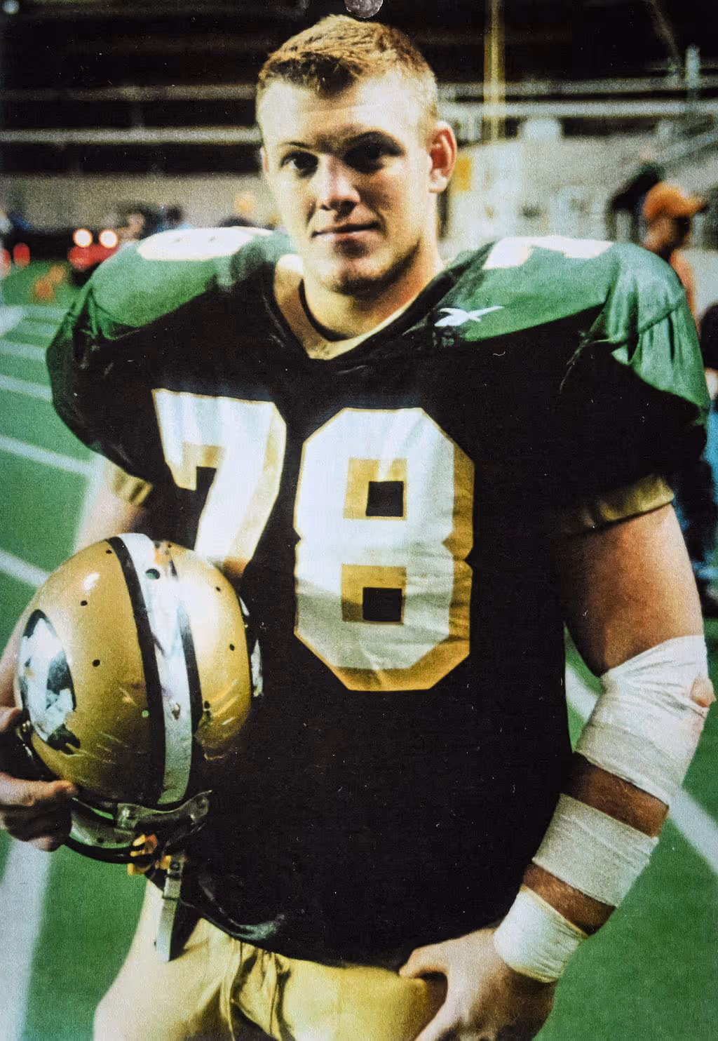 Young Paul Bondar football player wearing a black and green jersey number 78 holding a gold helmet, standing on a football field.