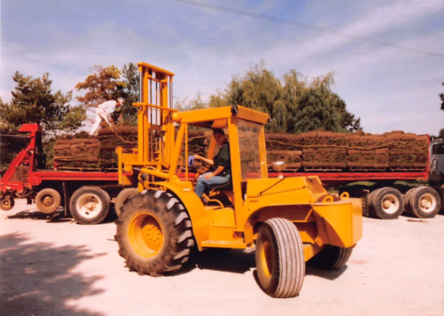 Paul Bondar operating a yellow forklift with a truck loaded with stacked sod rolls in the background.