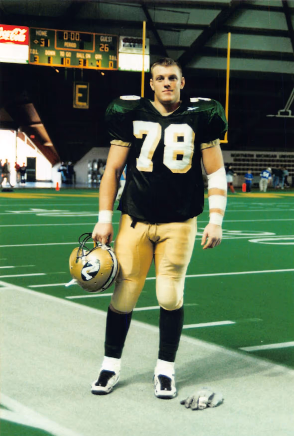 Paul Bondar wearing number 78 in black and gold uniform holding a helmet, standing on a football field.