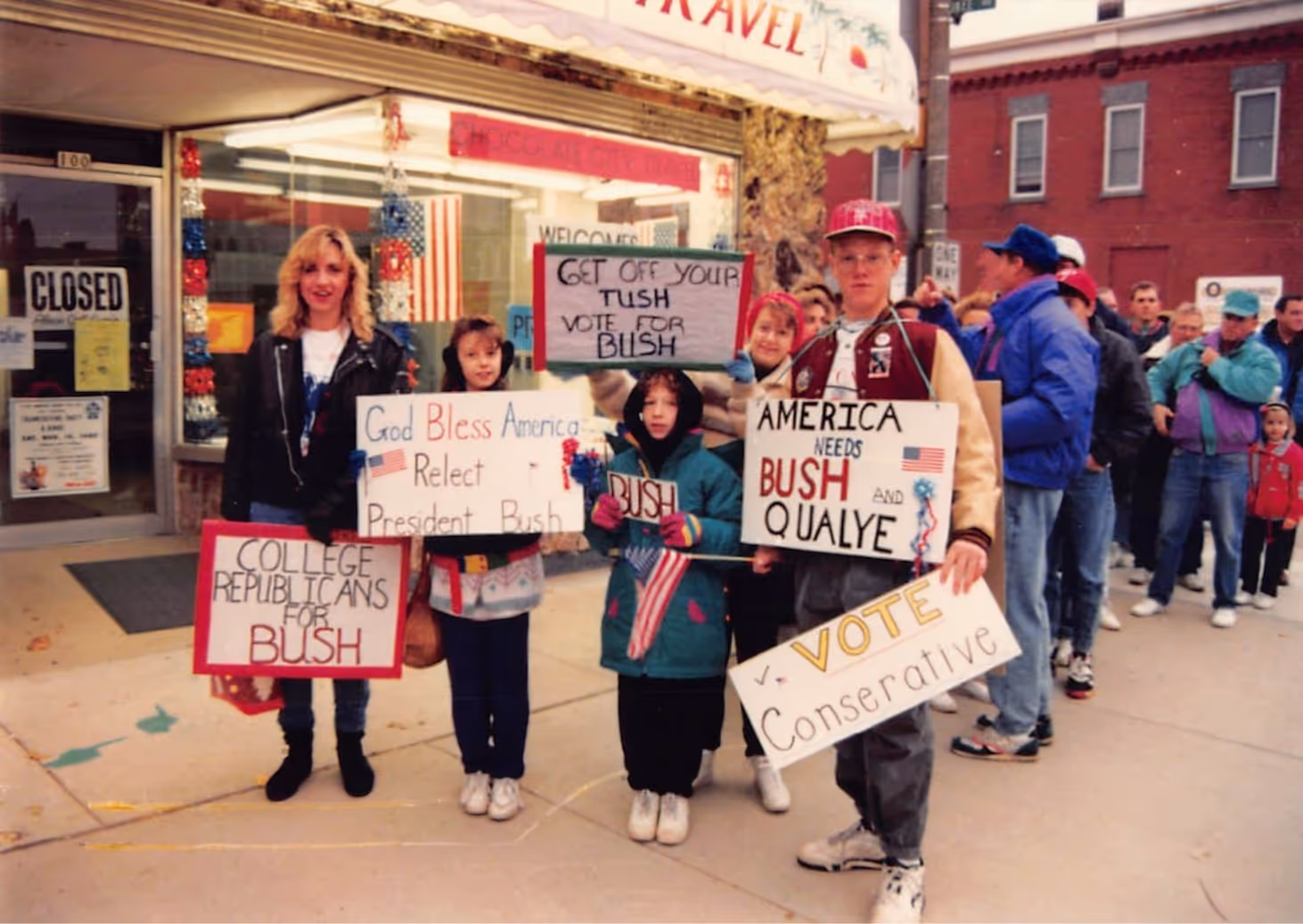 Group of young people holding signs supporting President Bush and conservative voting outside a store with an American flag in the window.