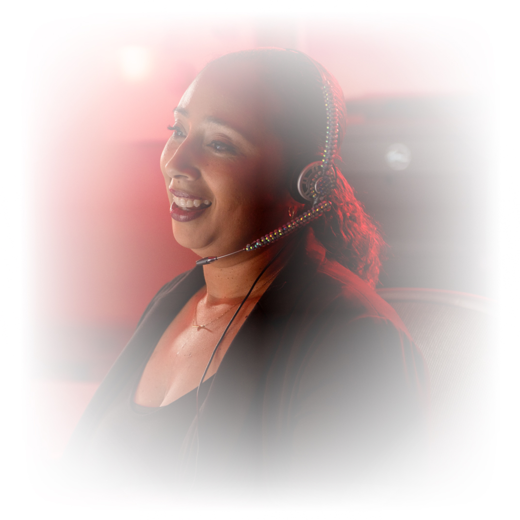 Smiling woman wearing a headset, engaged in a conversation, with a soft red background.