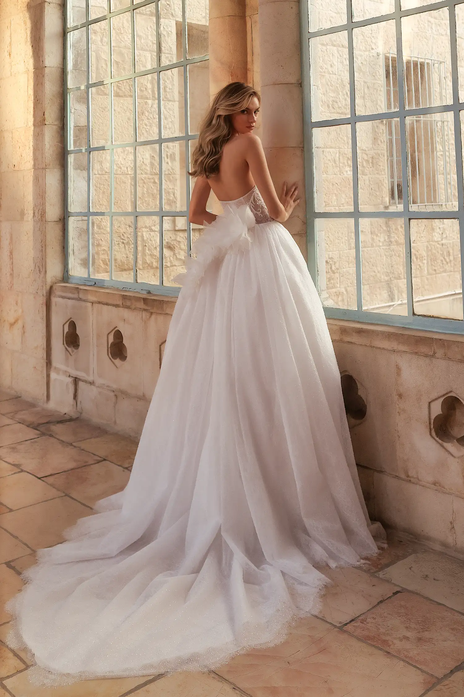 Strapless ballgown fully beaded with water crystals, with sheer bodice, water crystal appliqué, and chantilly lace handmade dimensional flowers at back waistline. Shown with chantilly lace and water crystal gauntlet gloves.
