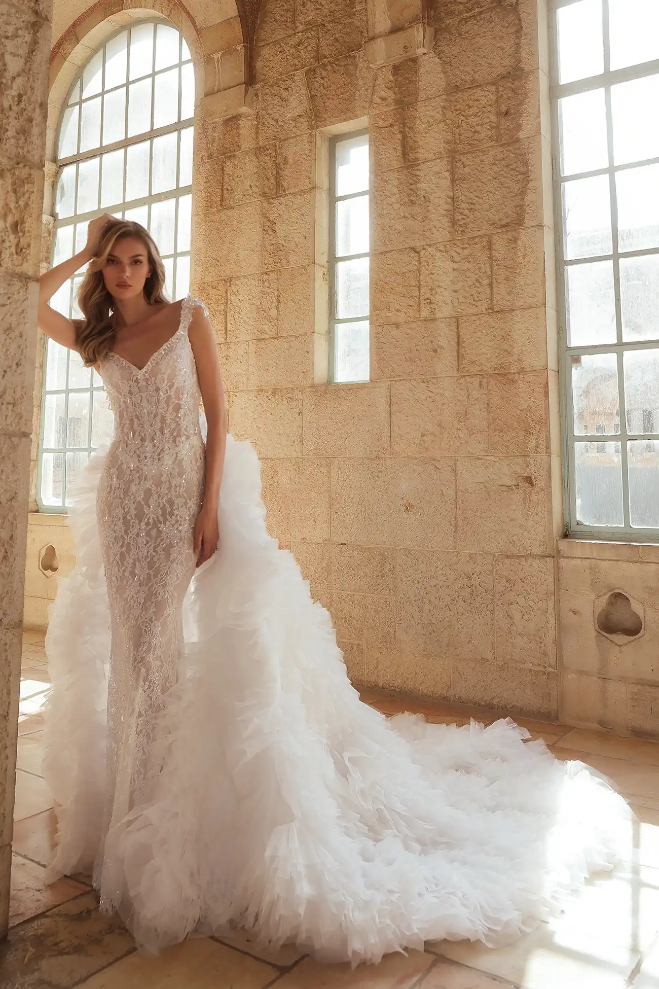 Hand-beaded chantilly lace sheath gown with portrait neckline embellished with water crystal droplets. Shown with detachable train in handmade organza flowers.