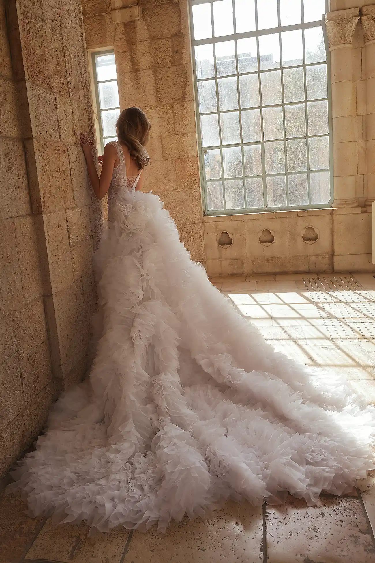 Hand-beaded chantilly lace sheath gown with portrait neckline embellished with water crystal droplets. Shown with detachable train in handmade organza flowers.