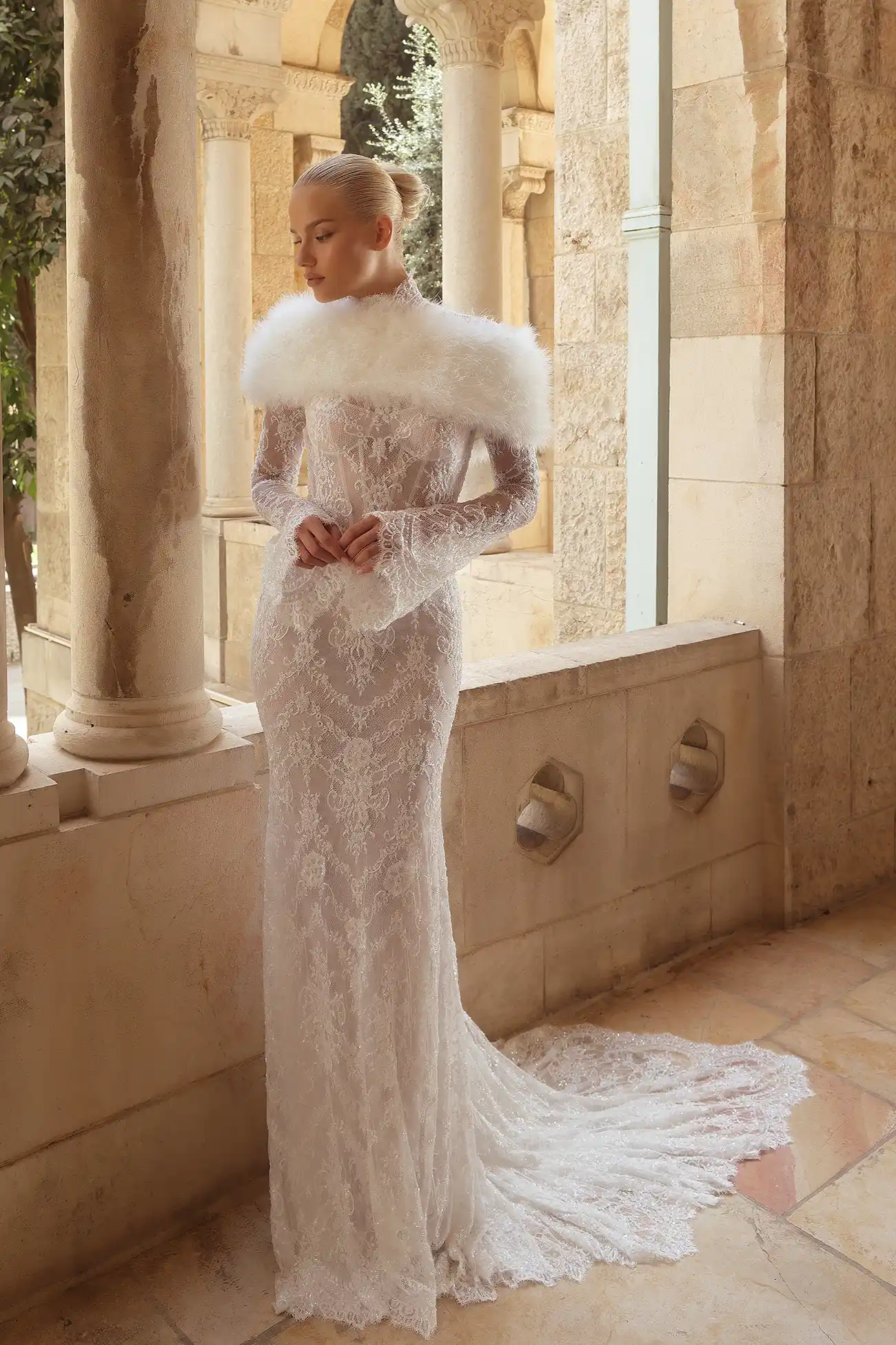 Hand-beaded chantilly lace sheath gown with high neckline, long bell sleeves, and sheer open back with water crystal tassels.