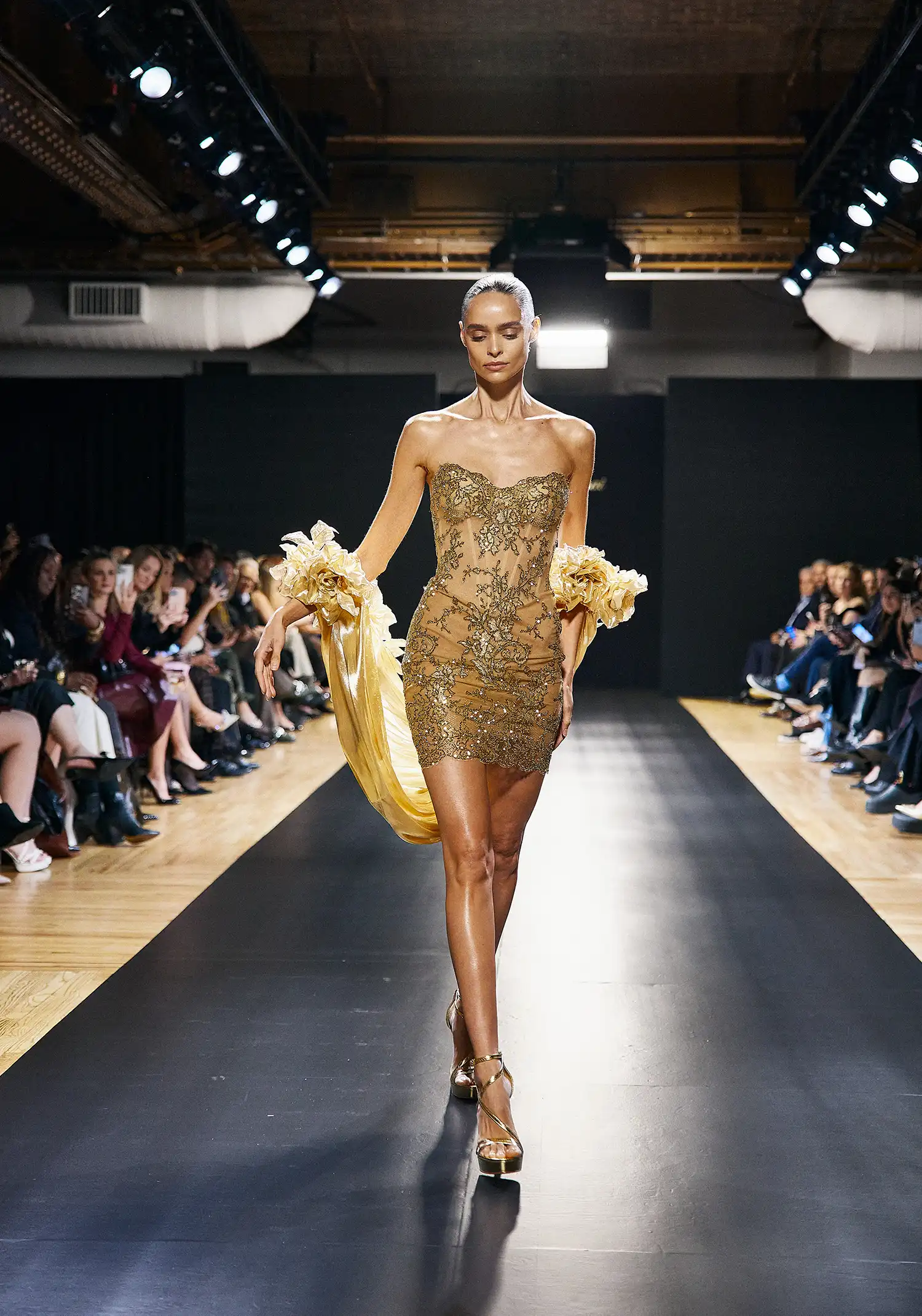 Strapless minidress in gold metallic chantilly lace, fully hand-embellished in gold crystals. Shown with liquid gold stole with handmade dimensional roses.