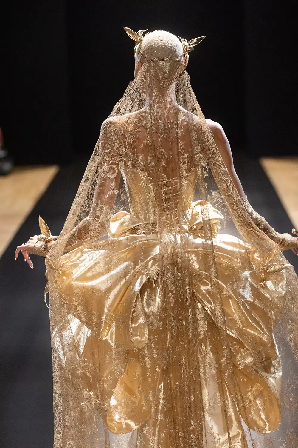 Strapless liquid gold fit-and-flare gown with basque waist accented with handmade dimensional roses, golden hummingbirds, and a large signature Pnina bow at back, shown with gold metallic chantilly lace gloves and veil.