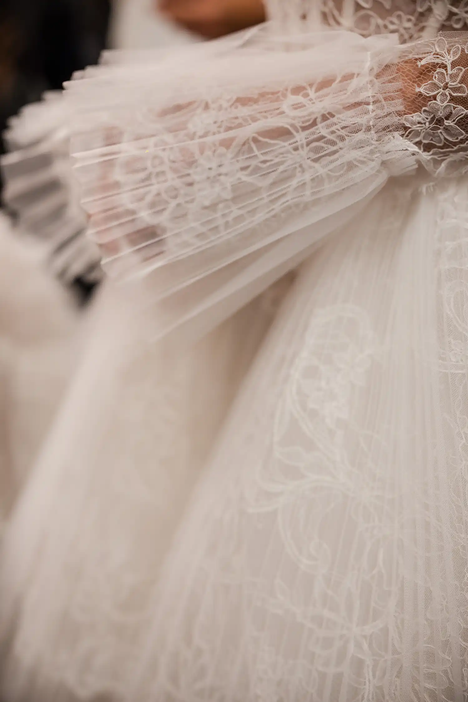 Strapless sweetheart ballgown in alençon lace and sunray pleated tulle, with structural lace and tulle ruffle skirt. Shown with cathedral-length veil with alençon lace border and lace gauntlet gloves with pleated tulle cuff detail.
