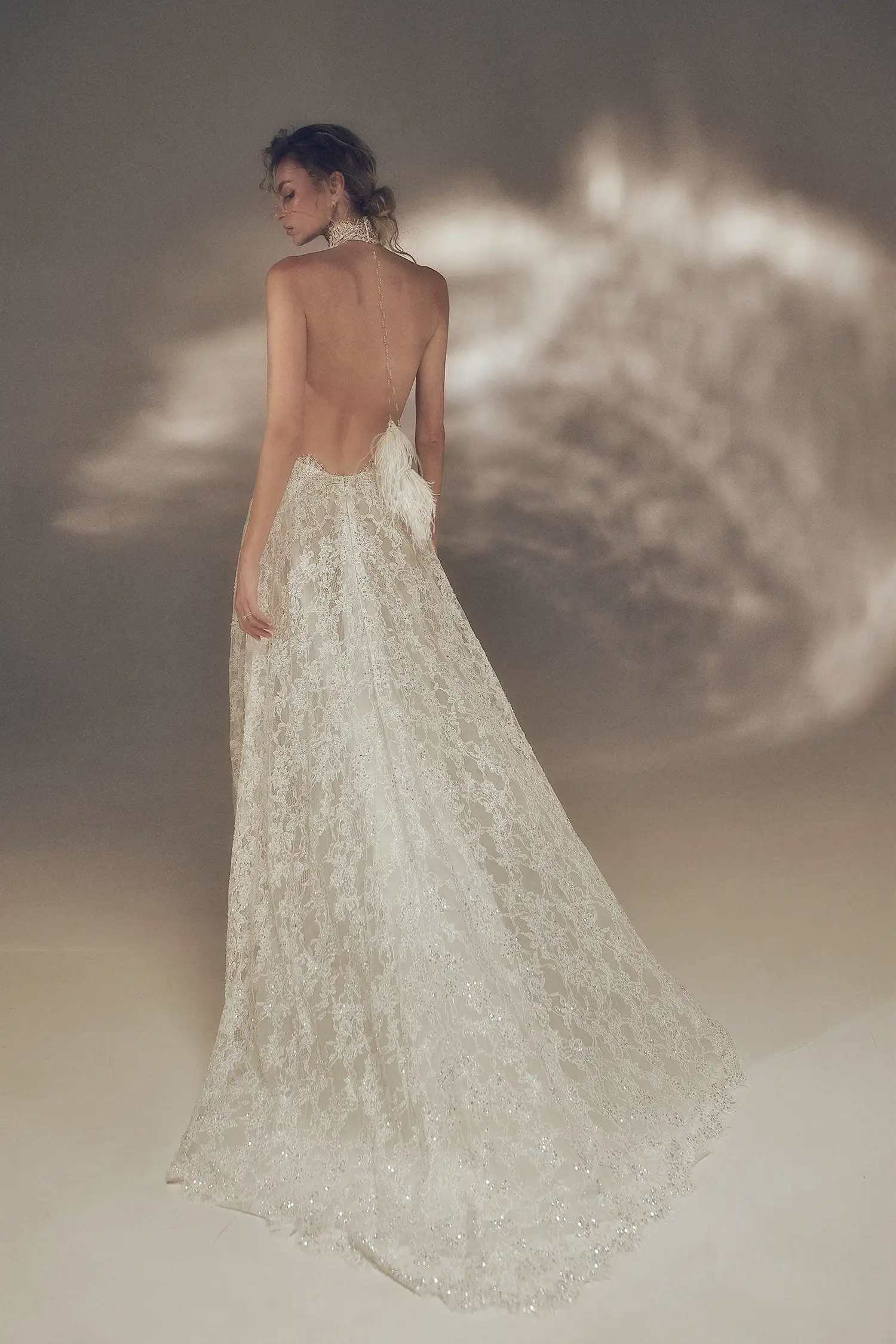 Hand-beaded chantilly lace A-line halter gown with open back and hanging clear crystal and ostrich feather tassel detail.
