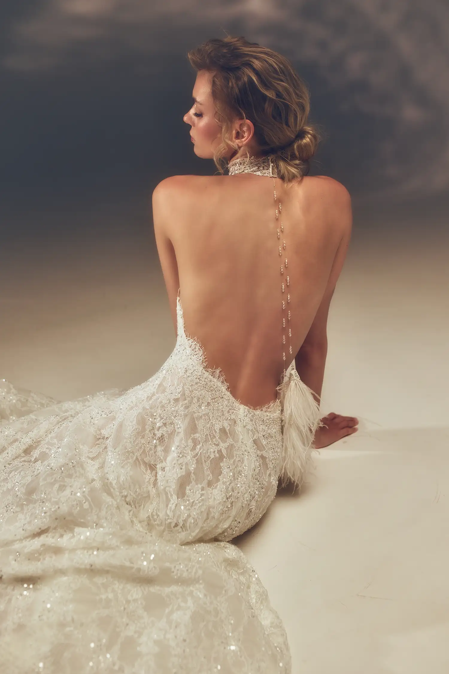 Hand-beaded chantilly lace A-line halter gown with open back and hanging clear crystal and ostrich feather tassel detail.