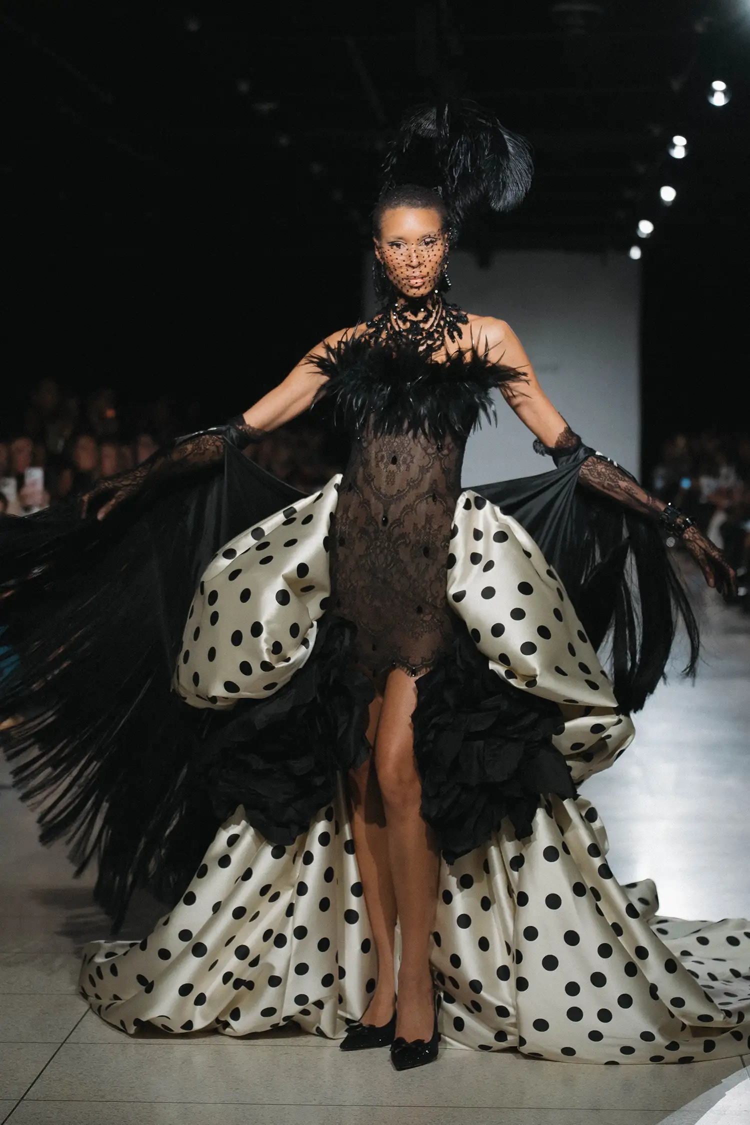 Black chantilly lace minidress with feather trim and black crystal droplets, shown with ivory and black polka-dot pickup overskirt with handmade oversized taffeta roses, black chantilly lace gloves, and hand painted black satin fringe shawl.