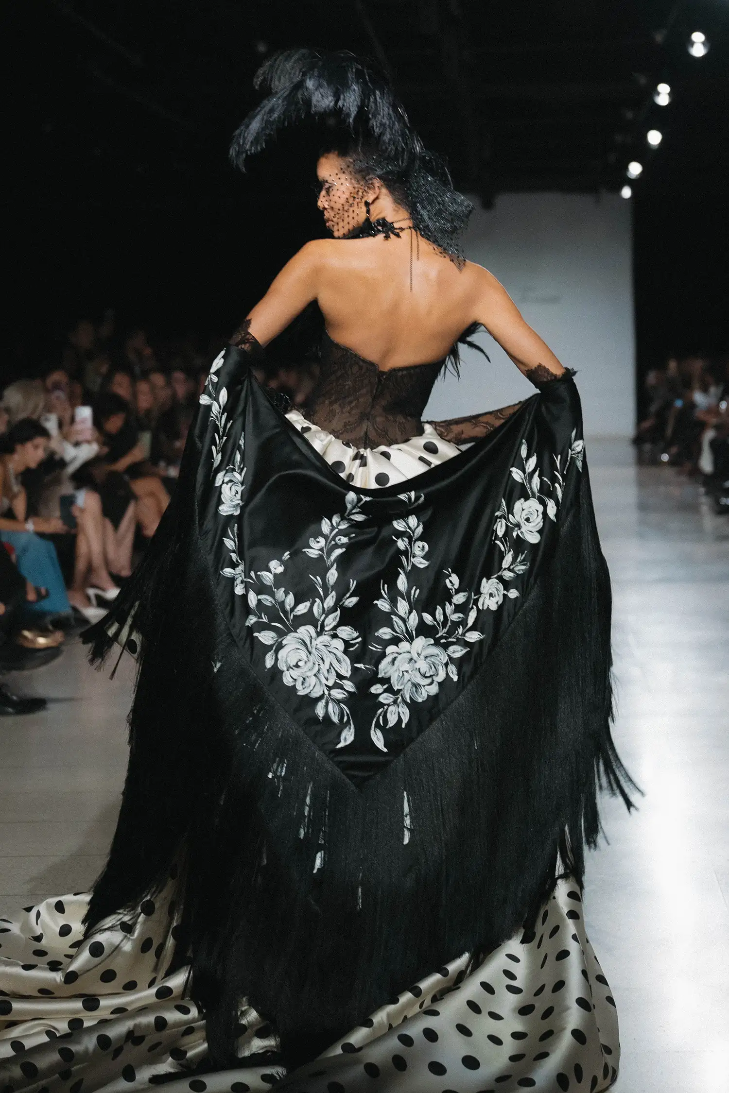 Black chantilly lace minidress with feather trim and black crystal droplets, shown with ivory and black polka-dot pickup overskirt with handmade oversized taffeta roses, black chantilly lace gloves, and hand painted black satin fringe shawl.