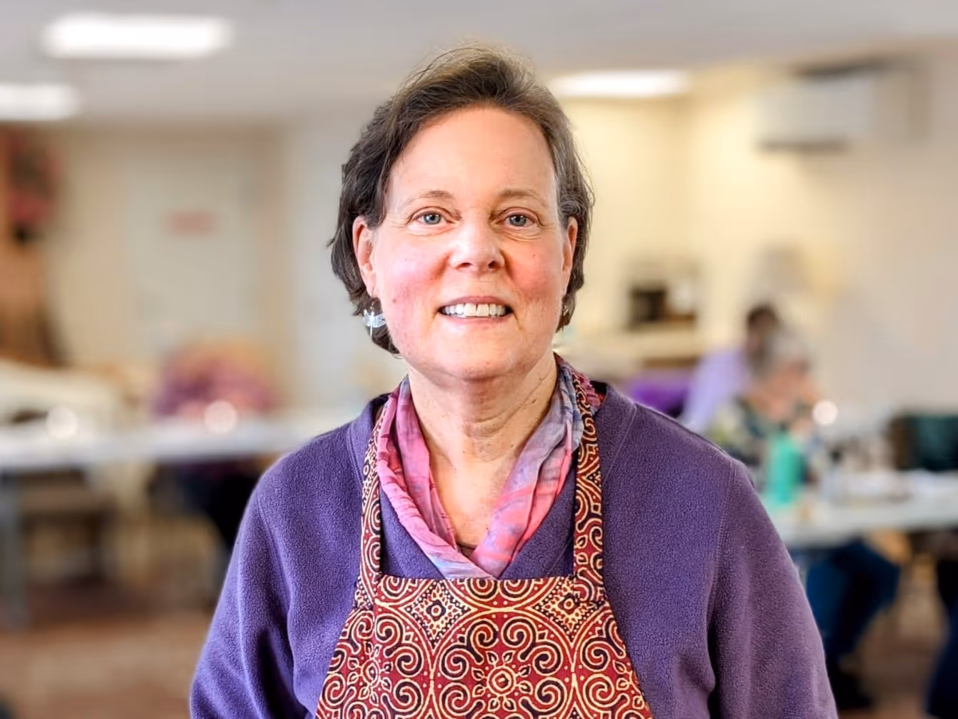 A photo of a woman in a purple sweater and apron, Rolling Ridge retreat leader