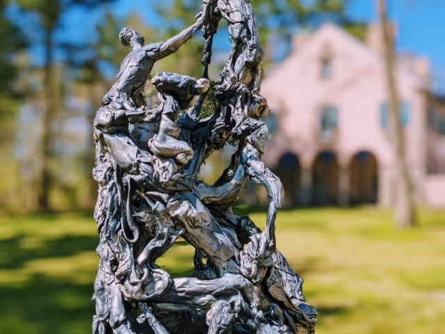 A close up photo of a statue by artist Mico Kaufman, with Rolling Ridge Main House buildings out of focus in the background